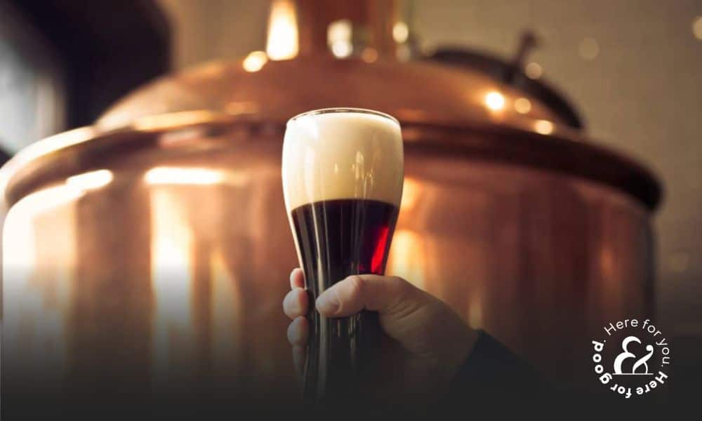 Brewer holding glass of bitter ale beer at brewery