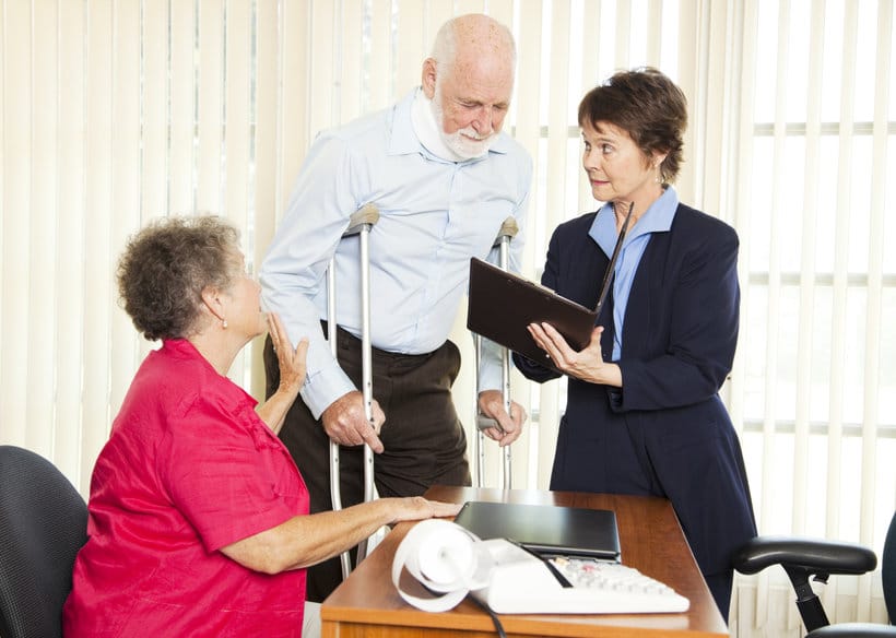 A lawyer showing a document to an elderly man on crutches, while his wife was sitting