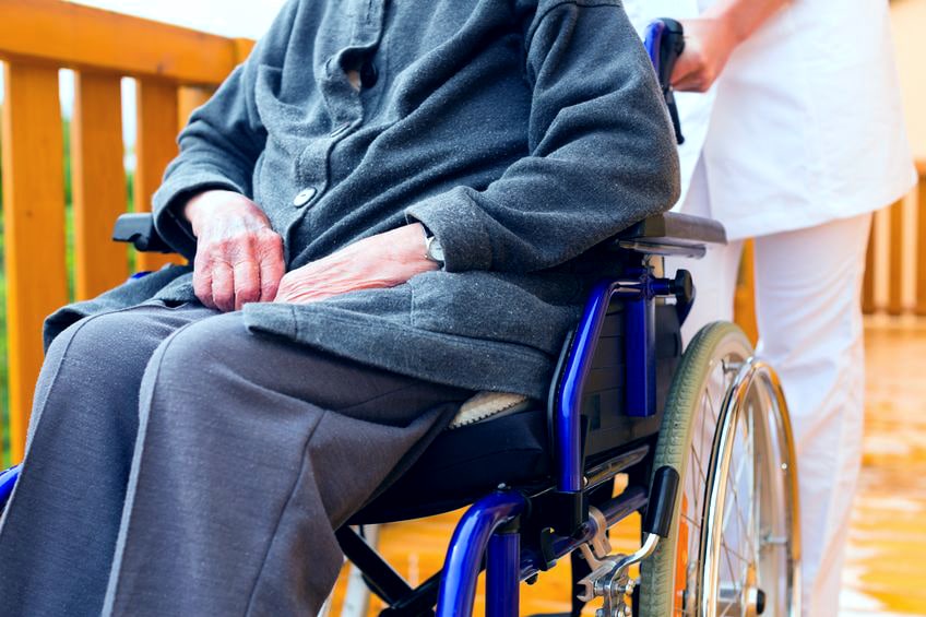 An elderly woman on a wheel chair being pushed by a nurse