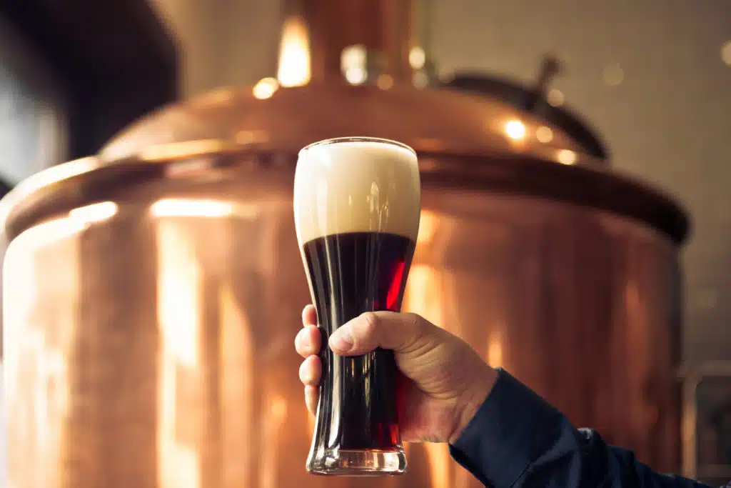 Brewer holding glass of bitter ale beer at brewery