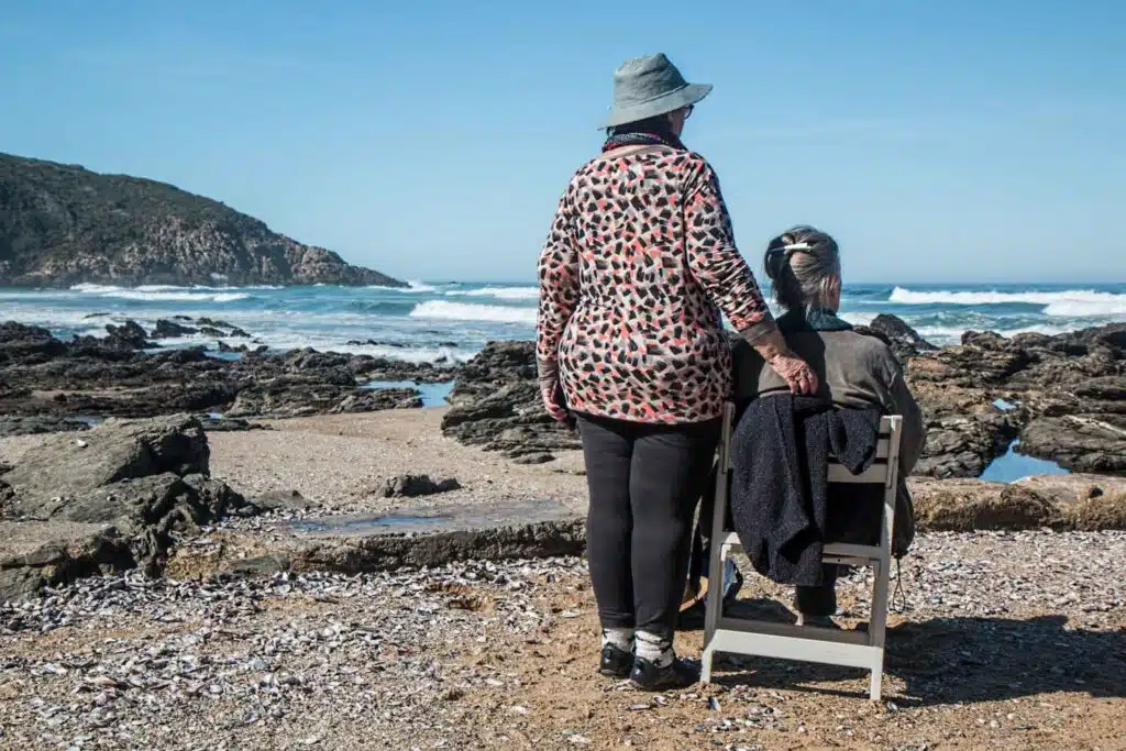A woman sitting by the sea and another standing by her