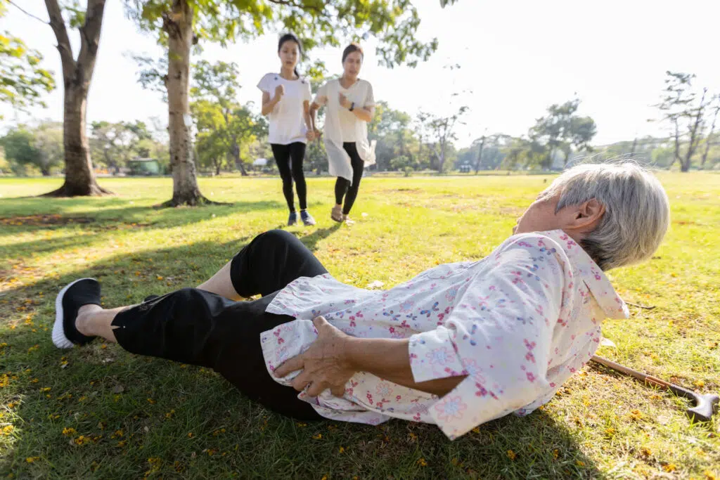 an elderly woman with a cane who has slipped and fallen on the ground while her granddaughters rush to help her