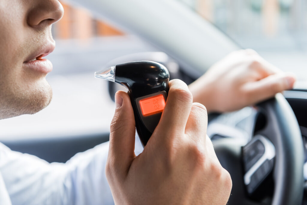 partial view of man blowing into breathalyzer while sitting in car, blurred background,stock image