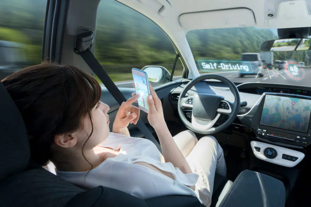 a woman using her cell phone will sitting in the driver's seat of a self-driving car