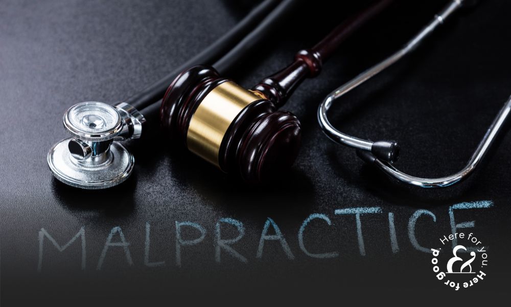A gavel and stethoscope on a table with a clipboard that reads malpractice