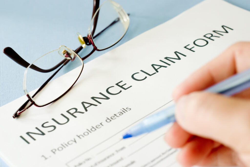 a person's hand filling out an insurance claim form on a table