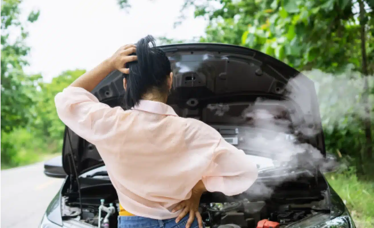 Woman with left hand on her head looking at the engine of her car