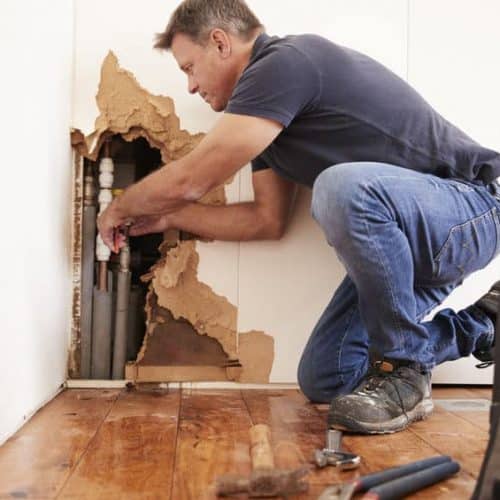 Plumber fixing the water pipe that burst inside a wall