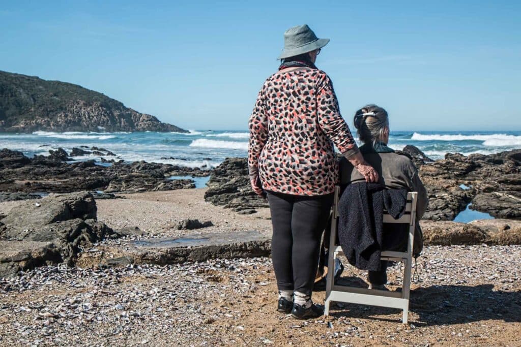 A woman sitting by the sea and another person standing by her