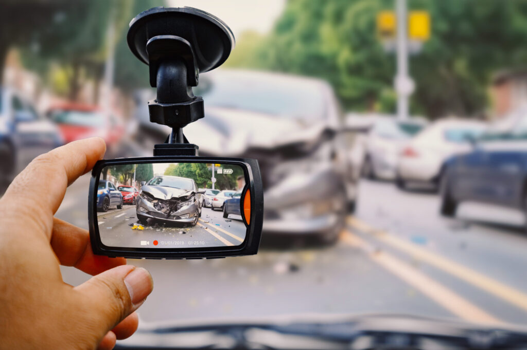 a hand touching a dash cam on a car windshield that features a car accident that happened in front of the car