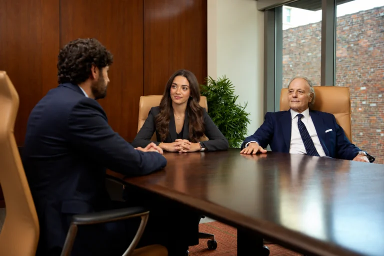 Three attorneys, Khalil Farah, Rania, and Eddie Farah, are sitting around a wooden conference table in a meeting room during a client or case discussion.